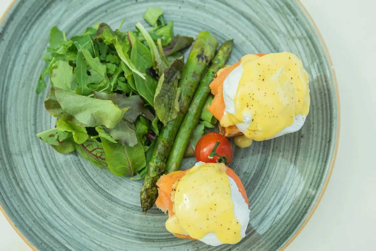 Delicious eggs benedict with hollandaise sauce, asparagus, and fresh salad on a plate.